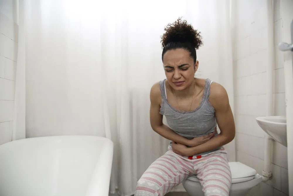 Woman sitting on the toilet holding her stomach in discomfort