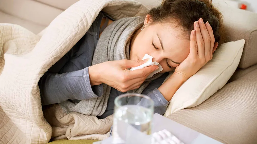 Woman in bed under a duvet blowing her nose into a tissue