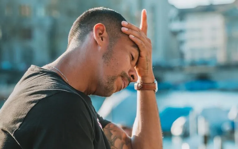 Man outdoors holding his hand to his forehead with a headache