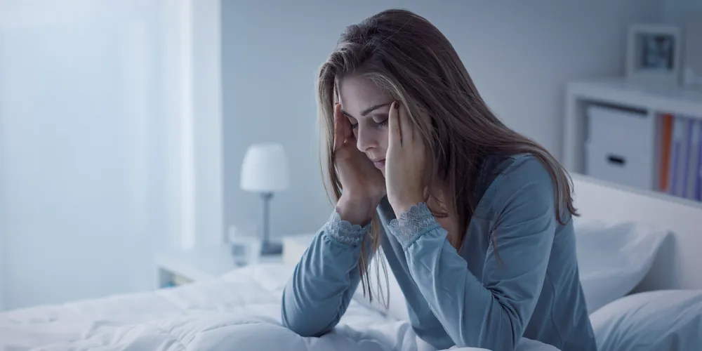 Woman sitting awake on the edge of the bed at night
