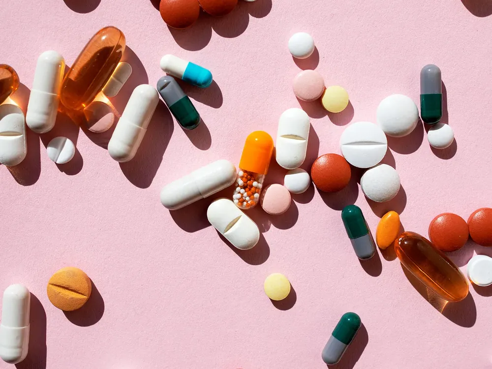 Assorted vitamin tablets and capsules scattered on a pink background