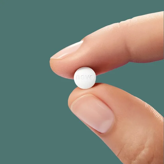 Small white oral tablet held between finger and thumb